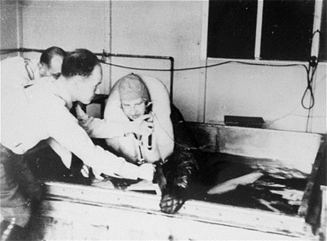 Жертву нацистского медицинского эксперимента погружают в ледяную воду в концентрационном лагере Дахау. Доктор Рашер наблюдает за экспериментом. Германия, 1942 г.