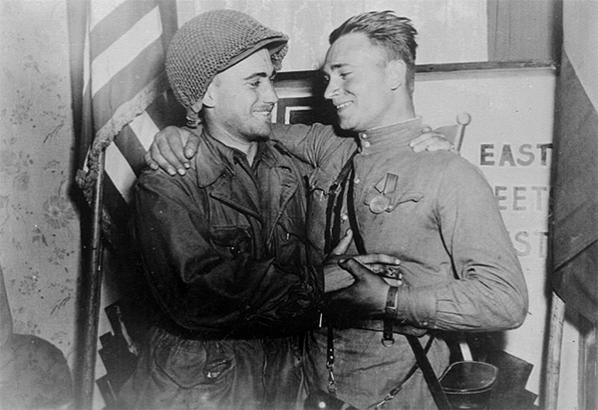 Второй лейтенант Робертсон и лейтенант Сильвашко на фоне надписи «Восток встречается с Западом», символизирующей историческую встречу союзников на Эльбе